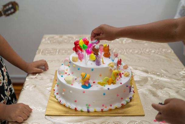 A closeup shot of hands burning the candles of a colorful birthday cake with cartoon characters - Foto, Imagen