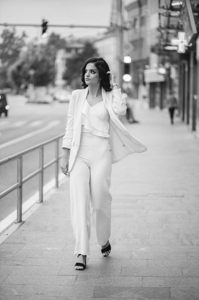 A grayscale of a gorgeous female in an elegant outfit walking in a street - Photo, image