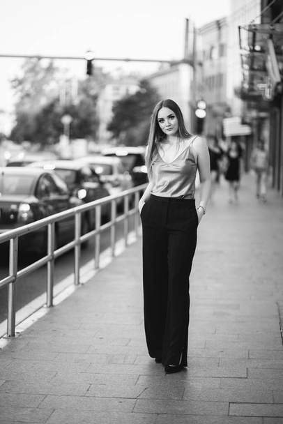 A grayscale of a gorgeous Caucasian female in stylish outfit posing in the street - Fotó, kép