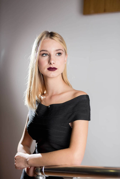 A beautiful blonde girl wearing a black dress with open shoulders and a dark red lipstick - Zdjęcie, obraz