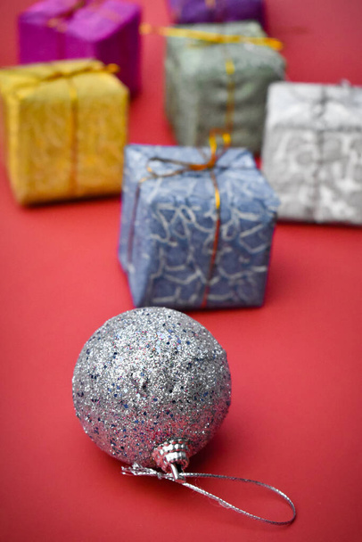 The small colorful present boxes with Christmas ball on red background - Photo, Image