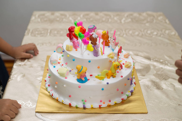 A closeup shot of hands on the table near the colorful birthday cake with cartoon characters - Fotografie, Obrázek
