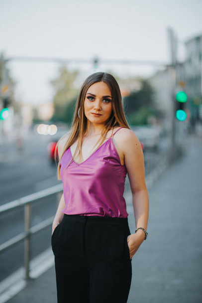 A gorgeous Caucasian female in stylish purple and black outfit posing in the street - Zdjęcie, obraz