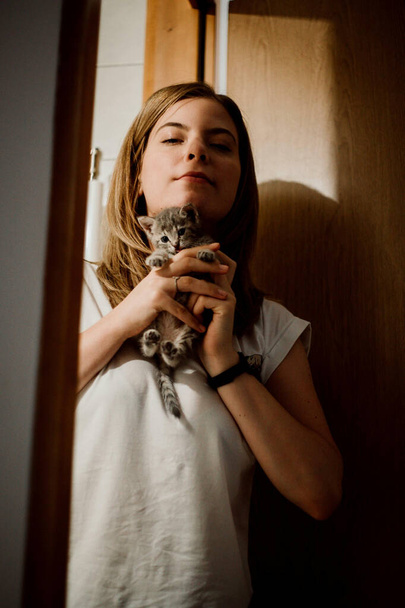 A beautiful shot of a blonde short-haired Caucasian woman holding an adorable little kitten - Foto, imagen