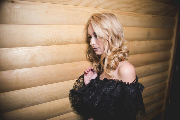 A beautiful blonde girl wearing a black dress with open shoulders - Φωτογραφία, εικόνα