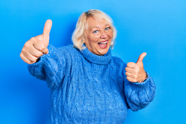 Μέση ηλικία ξανθιά γυναίκα φορώντας casual ρούχα έγκριση κάνει θετική χειρονομία με το χέρι, τους αντίχειρες επάνω χαμογελώντας και χαρούμενος για την επιτυχία. νικήτρια χειρονομία.  - Φωτογραφία, εικόνα