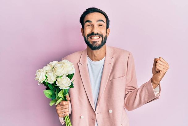 Çiçekleri tutan İspanyol genç adam gururla haykırıyor, zaferi kutluyor ve kollarını kaldırarak çok heyecanlanıyor.  - Fotoğraf, Görsel