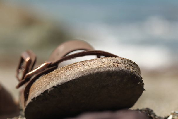 Sandal sitting on the sand of a beach close to the waterline and wave - Photo, Image