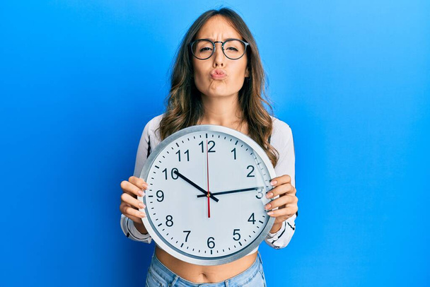 Young brunette woman holding big clock looking at the camera blowing a kiss being lovely and sexy. love expression.  - Foto, Imagem