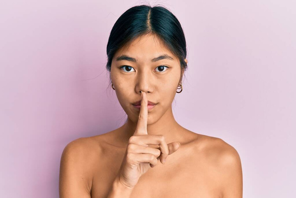 Fiatal kínai nő áll félmeztelenül, és azt mutatja, hogy a bőre csendre vágyik, ujjal a száján. csend és titkos koncepció.  - Fotó, kép