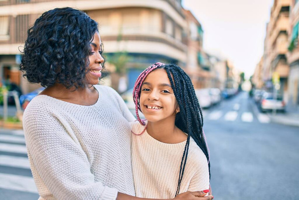 Прекрасна афро-американська мати і дочка посміхаються, радіючи і обіймаючись. Стоїть з посмішкою на обличчі, стоячи біля міста.. - Фото, зображення