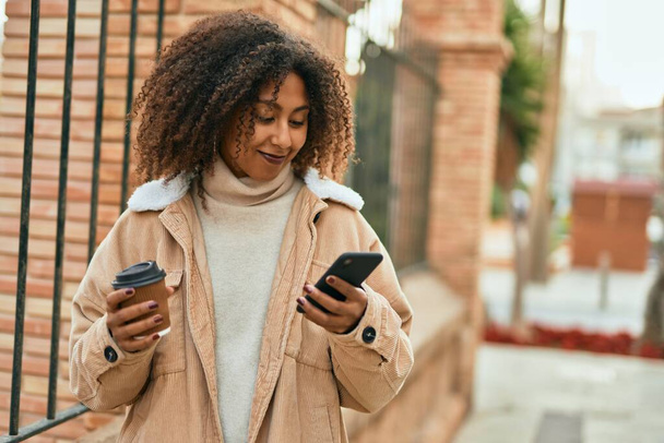 Junge Afroamerikanerin nutzt Smartphone und trinkt Kaffee in der Stadt. - Foto, Bild