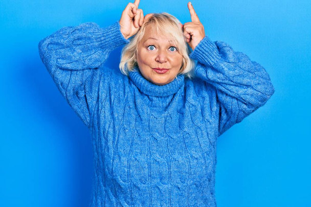 Femme blonde du moyen âge portant des vêtements décontractés faisant un geste drôle avec le doigt sur la tête comme des cornes de taureau  - Photo, image