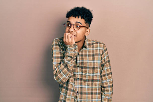 Young african american man wearing casual clothes and glasses looking stressed and nervous with hands on mouth biting nails. anxiety problem.  - Foto, afbeelding