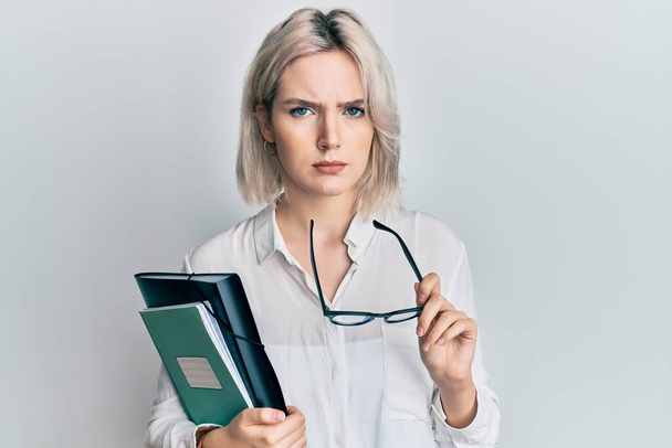 Young blonde girl reading a book and holding glasses skeptic and nervous, frowning upset because of problem. negative person.  - Photo, Image