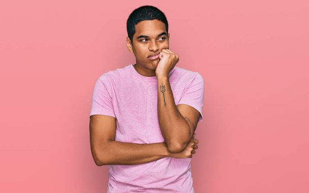Young handsome hispanic man wearing casual pink t shirt serious face thinking about question with hand on chin, thoughtful about confusing idea  - Valokuva, kuva