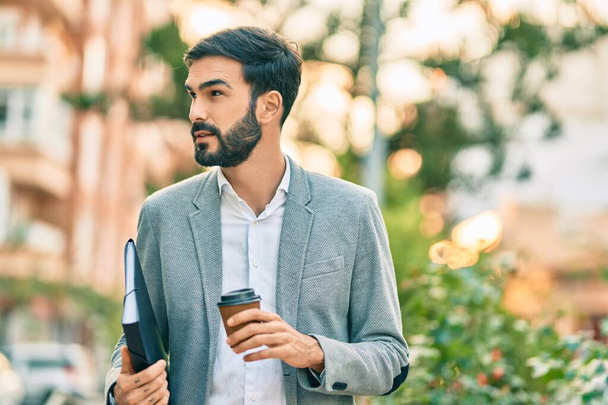 Jeune homme d'affaires hispanique souriant heureux boire emporter café à la ville. - Photo, image