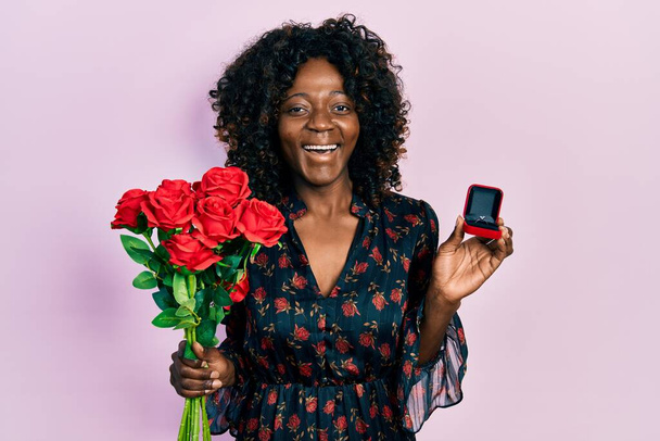 Młoda Afroamerykanka trzymająca bukiet kwiatów i pierścionek zaręczynowy uśmiechająca się i śmiejąca głośno, bo śmieszny żart.  - Zdjęcie, obraz