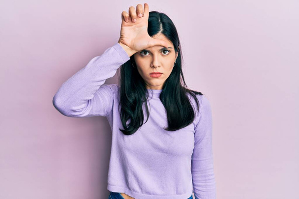 Young hispanic woman wearing casual clothes making fun of people with fingers on forehead doing loser gesture mocking and insulting.  - Photo, Image