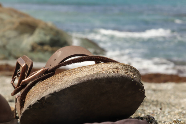 Sandalia sentada en la arena de una playa cerca de la línea de flotación y ola - Foto, Imagen