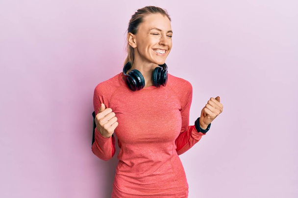Beautiful caucasian woman wearing sportswear and arm band excited for success with arms raised and eyes closed celebrating victory smiling. winner concept.  - Valokuva, kuva