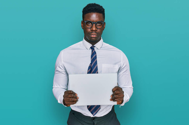 Handsome business black man holding blank empty banner thinking attitude and sober expression looking self confident  - Photo, image