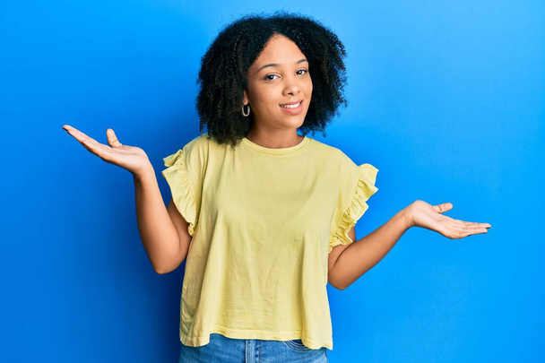 Junge afrikanische Amerikanerin in lässiger Kleidung, ahnungslos und verwirrt mit erhobenen Armen und Händen. Zweifelhaftes Konzept.  - Foto, Bild