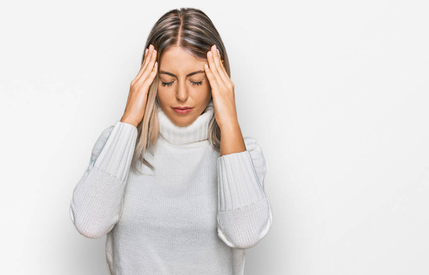 Beautiful blonde woman wearing casual turtleneck sweater with hand on head for pain in head because stress. suffering migraine.  - Photo, Image