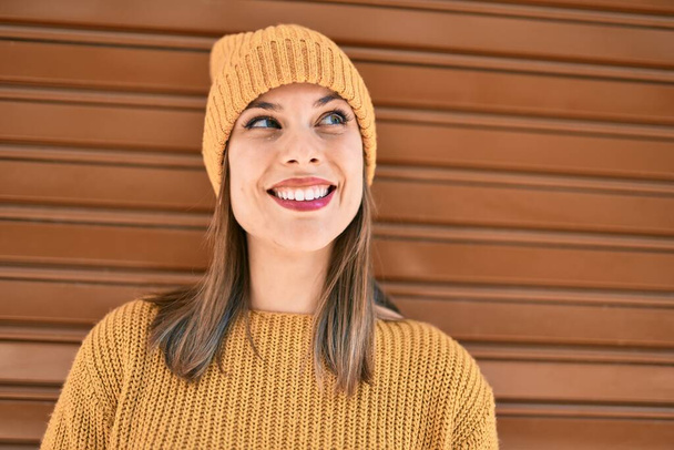 Kış tarzı giyinen genç sarışın kadın şehirde mutlu bir şekilde gülümsüyor.. - Fotoğraf, Görsel