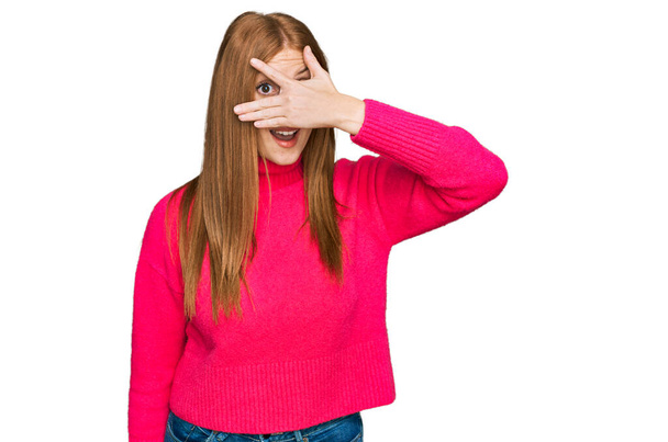 Mujer joven irlandesa que usa ropa casual asomándose en la cara y los ojos con la mano, mirando a través de los dedos con expresión avergonzada.  - Foto, Imagen