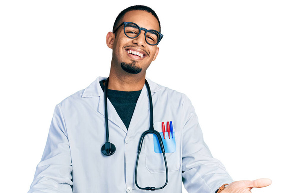 Giovane uomo afroamericano indossando uniforme medico e stetoscopio sorridente allegra offerta mani dando assistenza e accettazione.  - Foto, immagini