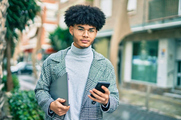 Giovane uomo d'affari afroamericano con espressione seria utilizzando lo smartphone in città. - Foto, immagini