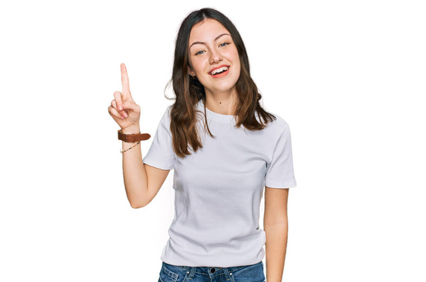 Молода красива жінка в повсякденній білій сорочці вказує пальцем на успішну ідею. вичерпаний і щасливий. номер один
.  - Фото, зображення