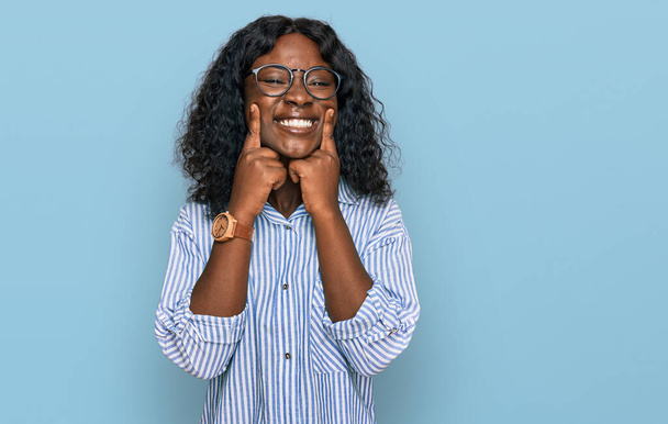 Όμορφη Αφρικανή νεαρή γυναίκα που φοράει casual ρούχα και γυαλιά χαμογελώντας με ανοιχτό στόμα, δάχτυλα που δείχνουν και αναγκάζοντας χαρούμενο χαμόγελο  - Φωτογραφία, εικόνα