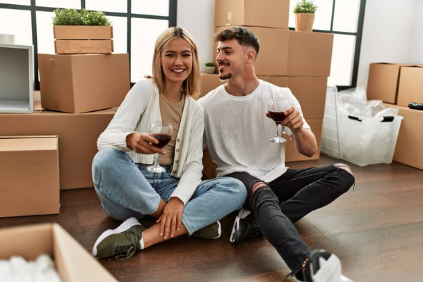 Kırmızı şarap kadehleriyle kadeh kaldıran beyaz bir çift yeni evlerinde oturuyor.. - Fotoğraf, Görsel