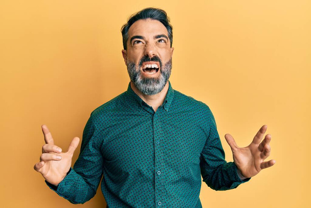 Middle age man with beard and grey hair wearing business clothes crazy and mad shouting and yelling with aggressive expression and arms raised. frustration concept.  - Zdjęcie, obraz