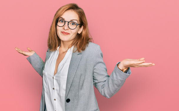 Young caucasian woman wearing business style and glasses clueless and confused expression with arms and hands raised. doubt concept.  - Photo, Image