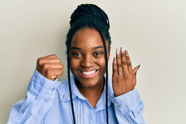 African american woman with braided hair wearing engagement ring screaming proud, celebrating victory and success very excited with raised arms  - Zdjęcie, obraz