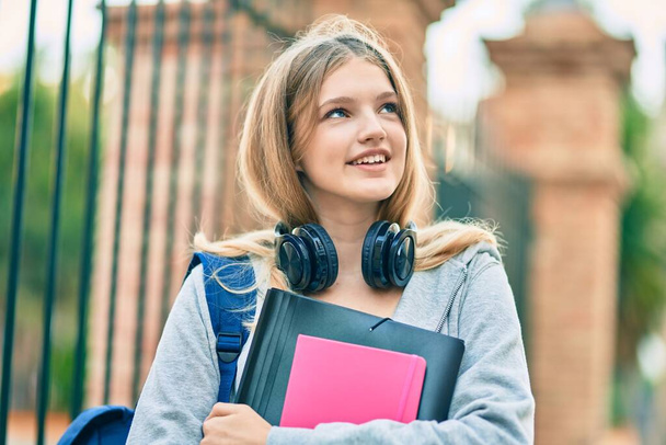Όμορφη καυκάσιος φοιτητής έφηβος χαμογελά χαρούμενος χρησιμοποιώντας ακουστικά στην πόλη. - Φωτογραφία, εικόνα