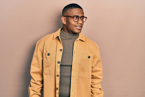 Young black man wearing casual clothes and glasses looking away to side with smile on face, natural expression. laughing confident.  - Photo, Image