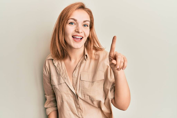 Молодая белая женщина в повседневной одежде улыбается с идеей или вопросом, показывая пальцем вверх со счастливым лицом, номер один  - Фото, изображение