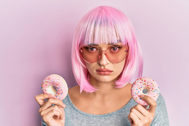 Young caucasian woman wearing pink wig holding donuts skeptic and nervous, frowning upset because of problem. negative person.  - Fotoğraf, Görsel