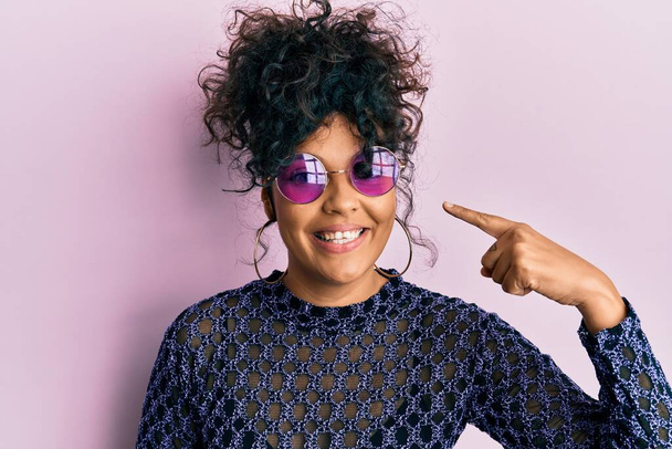 Young hispanic woman wearing cool sunglasses smiling happy pointing with hand and finger  - Foto, Imagem