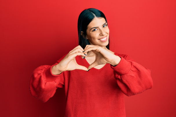 Fiatal spanyol nő alkalmi ruhát visel mosolygó szerelmes mutatja szív szimbólum és alakja kézzel. romantikus koncepció.  - Fotó, kép