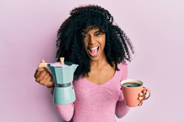 Αφροαμερικανή γυναίκα με αφρο μαλλιά πίνοντας ιταλικό καφέ να κλείνει το μάτι κοιτάζοντας την κάμερα με σέξι έκφραση, χαρούμενο και χαρούμενο πρόσωπο.  - Φωτογραφία, εικόνα