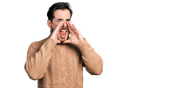 Young hispanic man wearing casual clothes shouting angry out loud with hands over mouth  - Foto, Bild