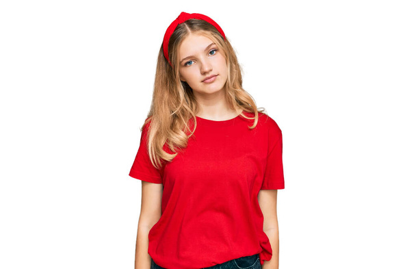 Gyönyörű fiatal kaukázusi lány, alkalmi piros pólóban, lazán, komoly arckifejezéssel. egyszerű és természetes nézi a kamerát.  - Fotó, kép