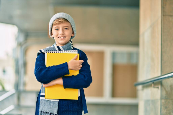 Adorable blond student kid smiling happy holding book at the school. - Valokuva, kuva