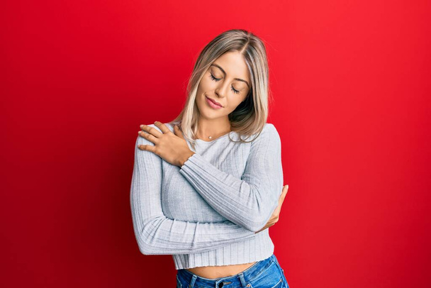Beautiful blonde woman wearing casual clothes hugging oneself happy and positive, smiling confident. self love and self care  - Photo, Image