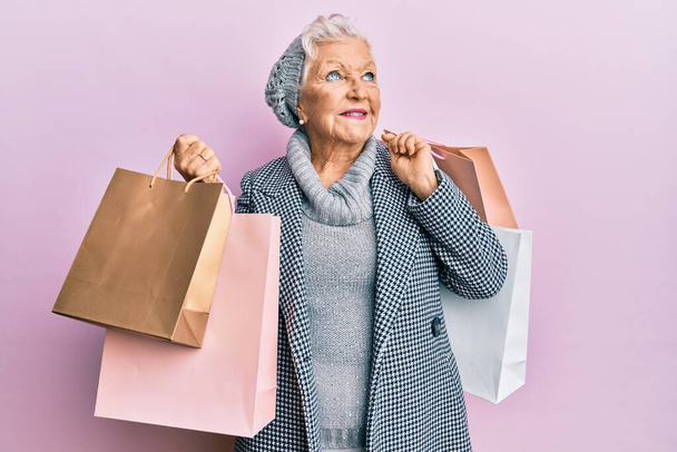 Senior grauhaarige Frau mit Einkaufstaschen lächelnd zur Seite schauen und wegstarren denken.  - Foto, Bild